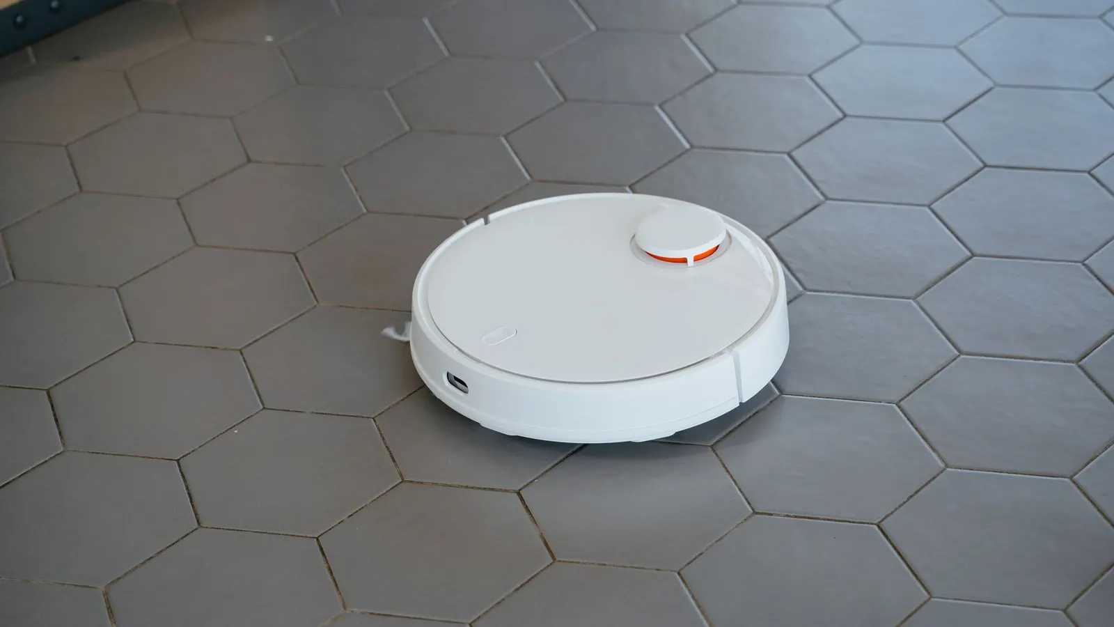 Aspirator robot alb cu senzor laser rotund pe o pardoseală cu plăci hexagonale gri
