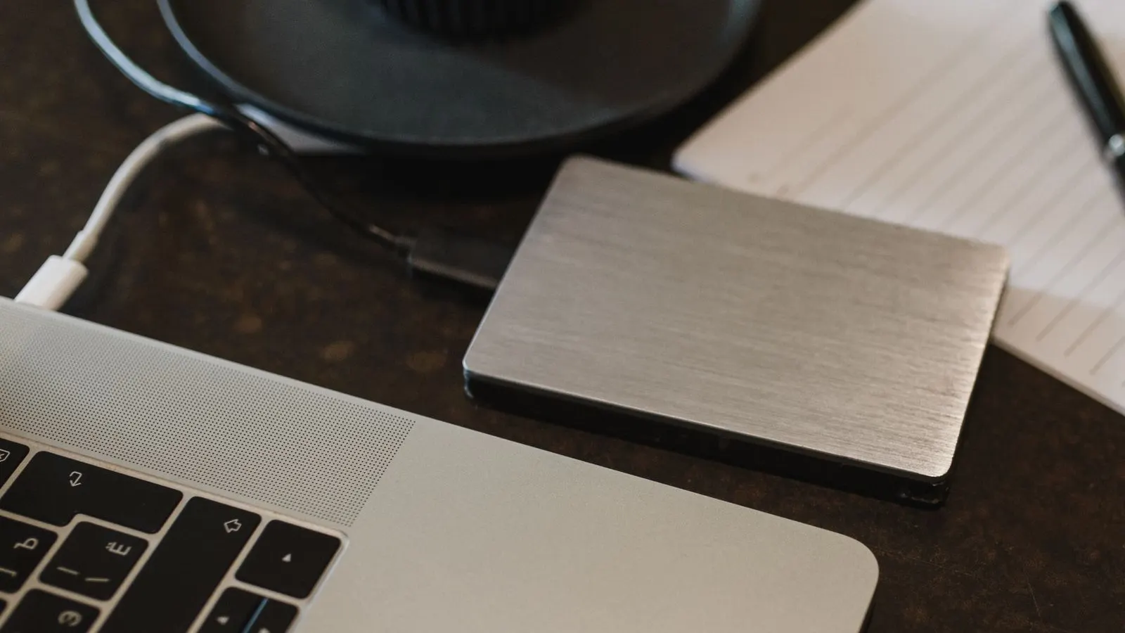 Disc extern conectat cu un cablu la un laptop, pe un birou închis la culoare
