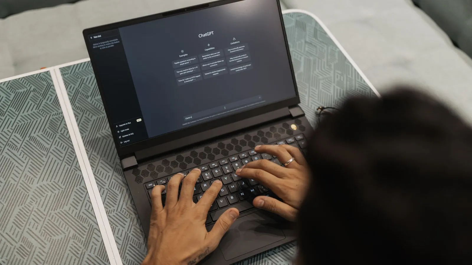 Mâini care tastează la un laptop cu interfața ChatGPT deschisă pe ecran