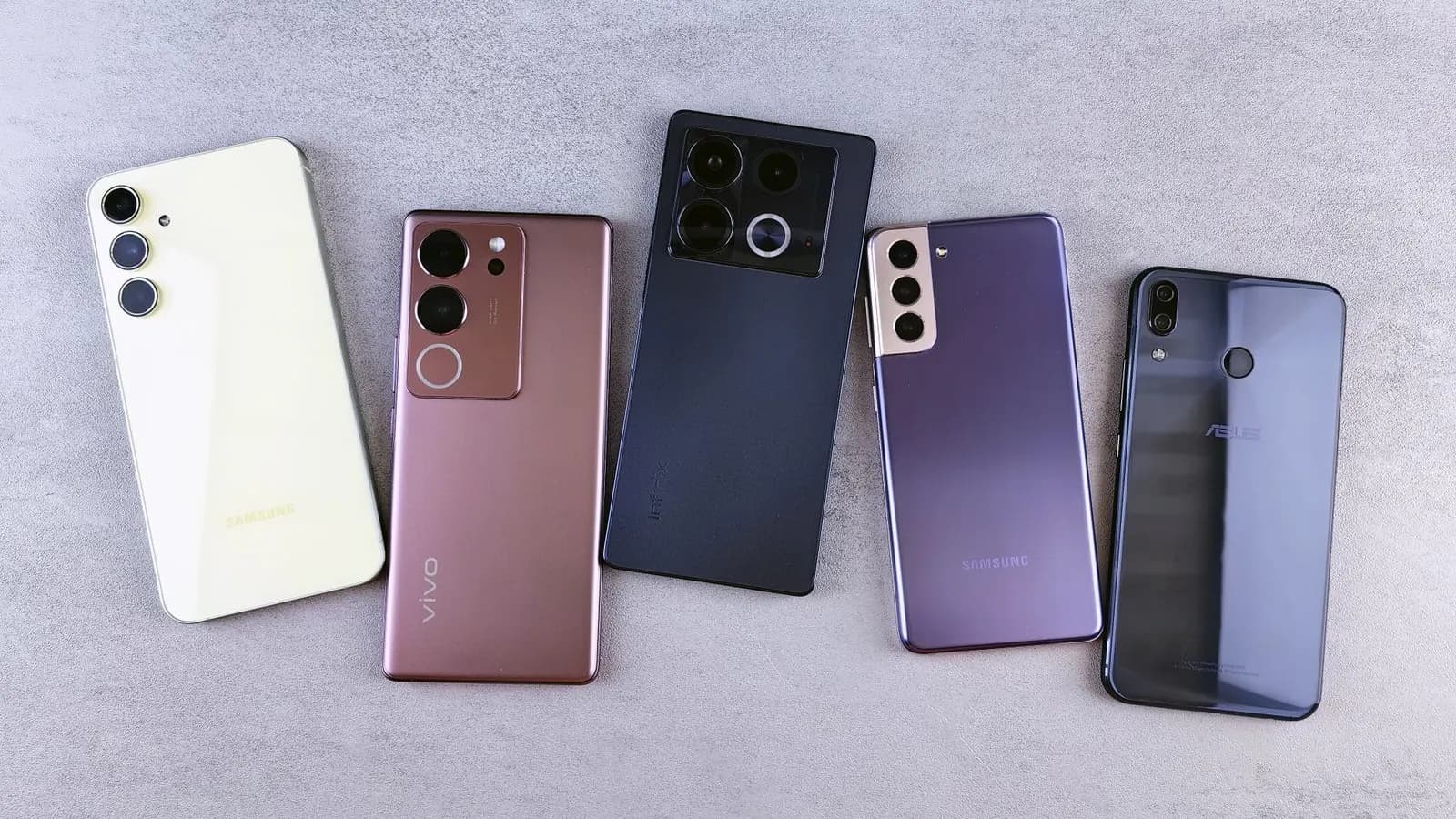Cinci smartphone-uri de mărci diferite așezate cu spatele în sus pe o masă gri