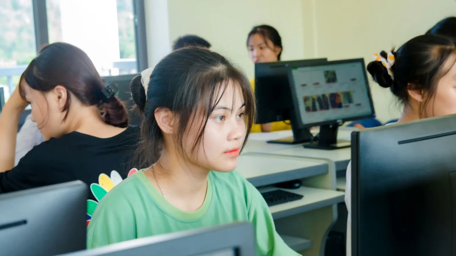 Tineri concentrați lucrează la calculatoare într-o sală de curs de informatică