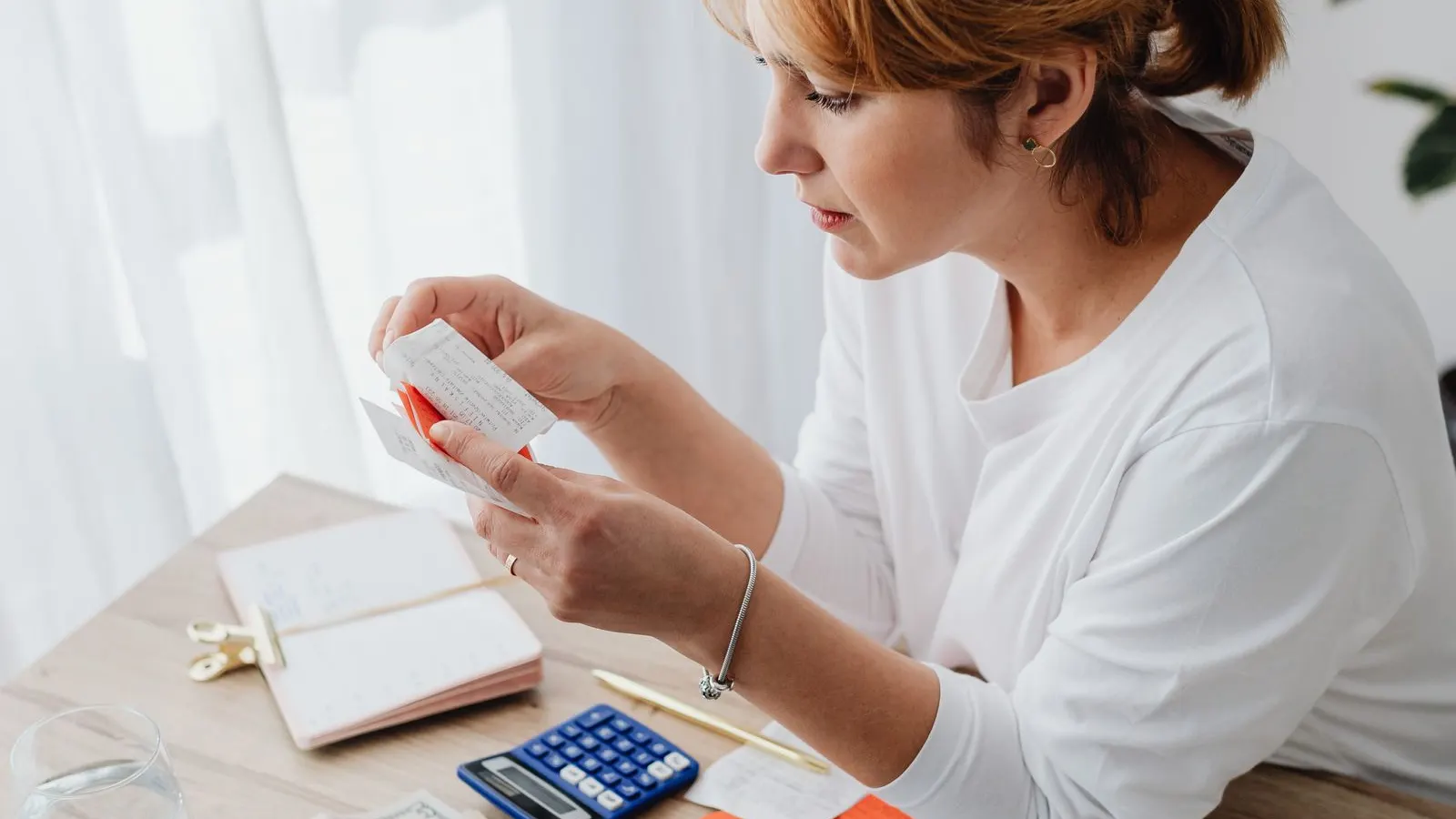 Femeie care verifică chitanțe la birou, lângă un calculator și un carnet