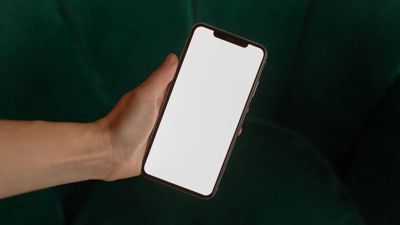 Mână care ține un smartphone cu ecran alb pe un fundal verde închis
