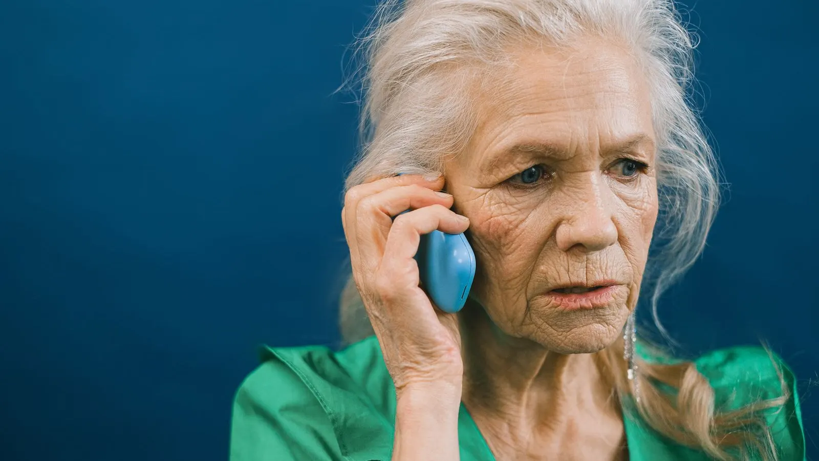 Femeie în vârstă, îngrijorată, vorbește la telefon pe un fundal albastru