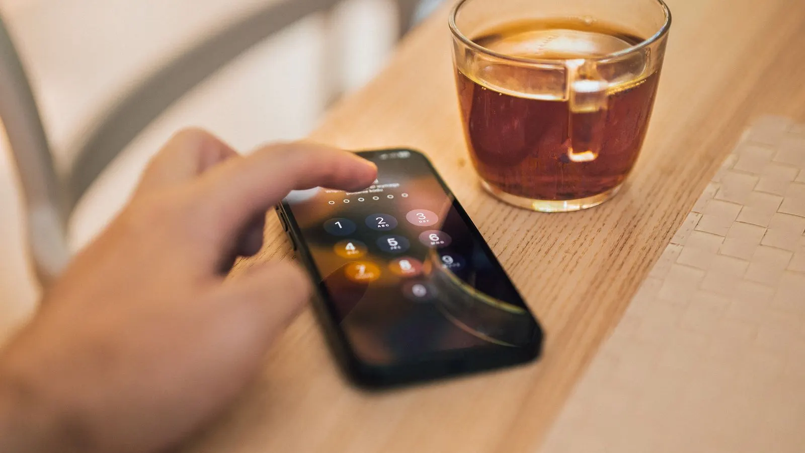 Mână care introduce codul de deblocare pe un telefon, lângă o cană de ceai