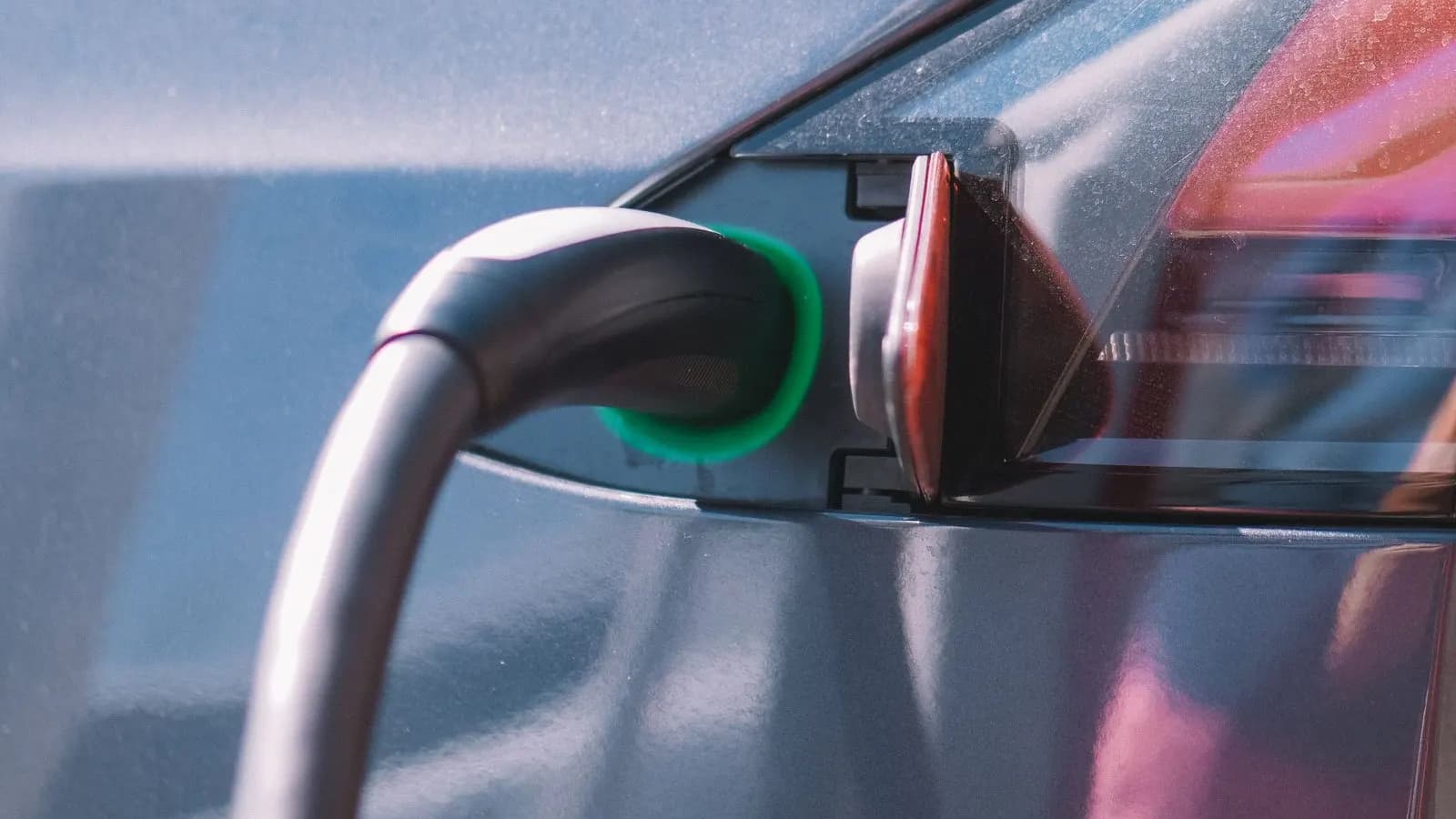 Cablu de încărcare conectat la portul unei mașini electrice gri, în prim-plan