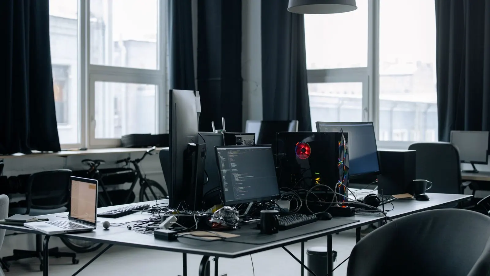 Birou de firmă IT cu monitoare pe care rulează cod, laptopuri și scaune goale