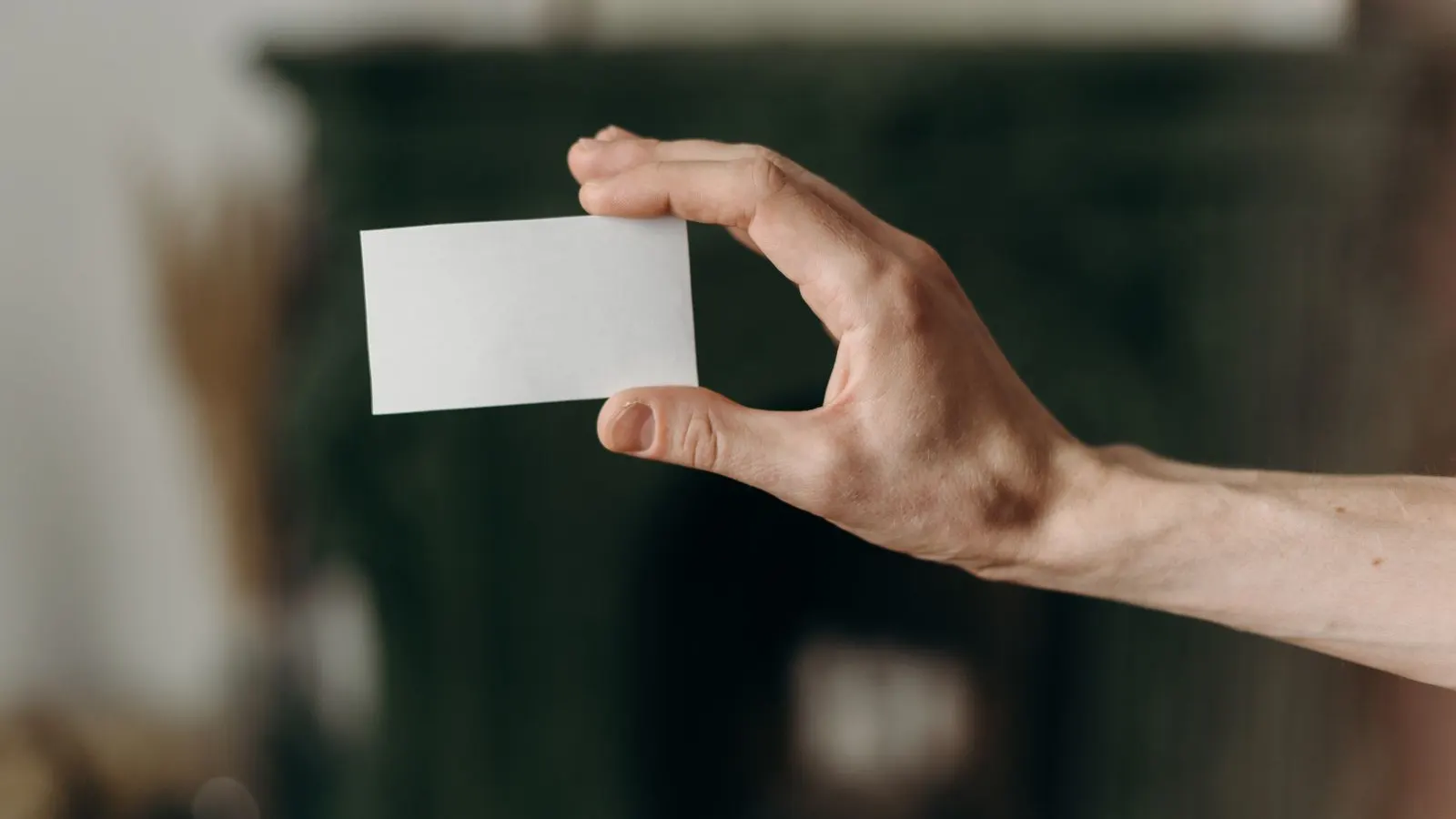 Mână care ține un card alb fără inscripții, pe un fundal întunecat