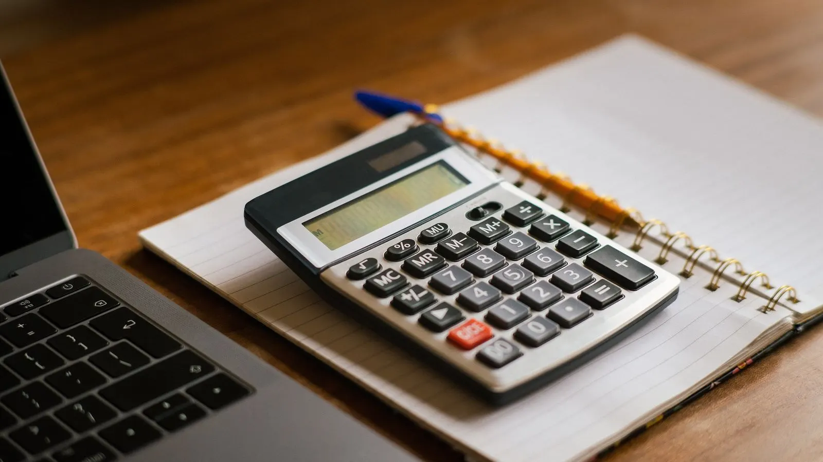 Calculator de birou pe un caiet deschis, lângă un laptop, pe o masă din lemn