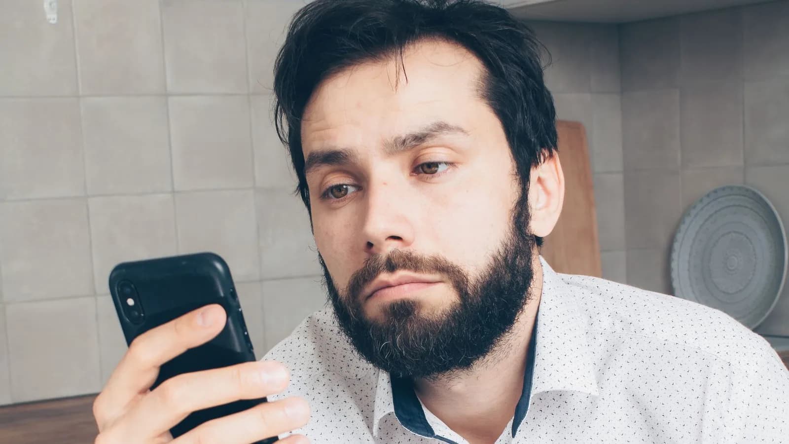 Bărbat dezamăgit se uită la ecranul telefonului pe care îl ține în mână