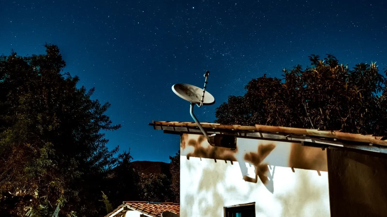 Casă la țară cu o antenă de satelit pe acoperiș, sub un cer plin de stele