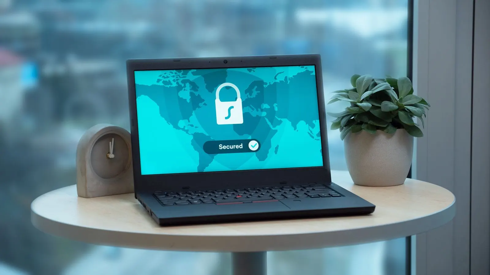 Laptop pe o masă rotundă, cu un lacăt și o hartă a lumii pe ecran
