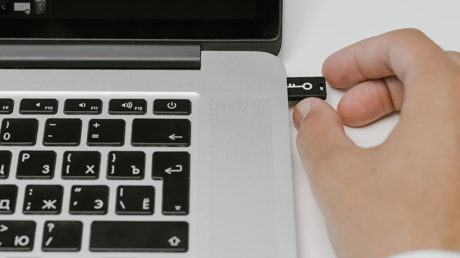 Mână care introduce un stick USB în portul lateral al unui laptop